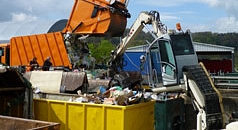 Das Foto zeigt ein Pressmüllfahrzeug beim Abladen auf dem Servicehof. Das Material wird direkt mit einem Bagger vor Ort verdichtet.