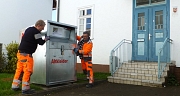 Mitarbeiter des DBM stellen einen Altkleidercontainer neben den Eingang des Ginseldorfer Bürgerhauses.