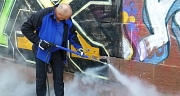 Das Foto zeigt einen Mann beim Beseitigen eines Graffitos auf einer Sandsteinmauer mit einem Hochdruckreiniger.