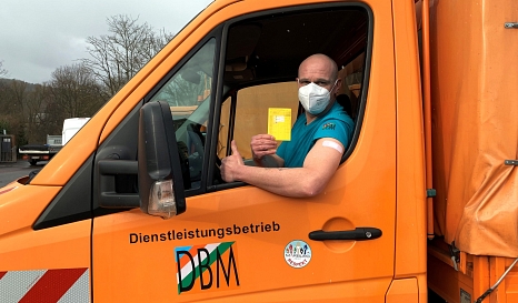 Das Foto zeigt einen Beschäftigten des DBM, der in einem Fahrzeug sitzt und einen Impfpass hoch hält. © DBM