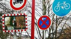 Das Foto zeigt verschiedene Schilder und einen Verkehrsspiegel an einem Mast.